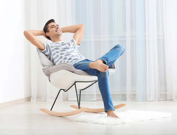 Молодий чоловік розслабляється на затишному кріслі в світлій кімнаті — стокове фото