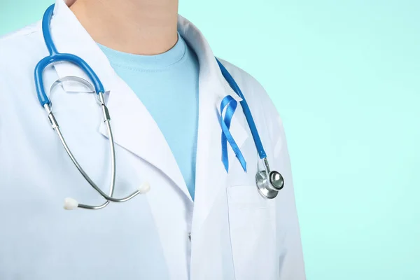 Doctor con cinta azul simbólica sobre fondo de color. Concepto de concienciación — Foto de Stock