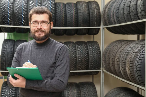 Venditore con appunti vicino pneumatici su rack in negozio di automobili — Foto Stock