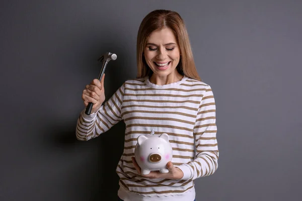 Young woman holding hammer over piggy bank on grey background — Stock Photo, Image