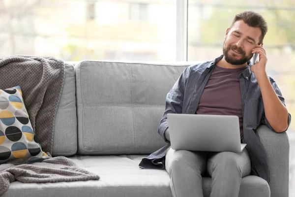 Homem maduro usando laptop e falando no telefone em casa — Fotografia de Stock