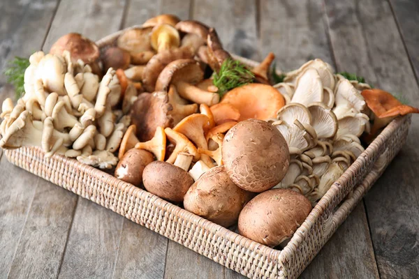 Weidenschale mit verschiedenen rohen Pilzen auf Holztisch — Stockfoto