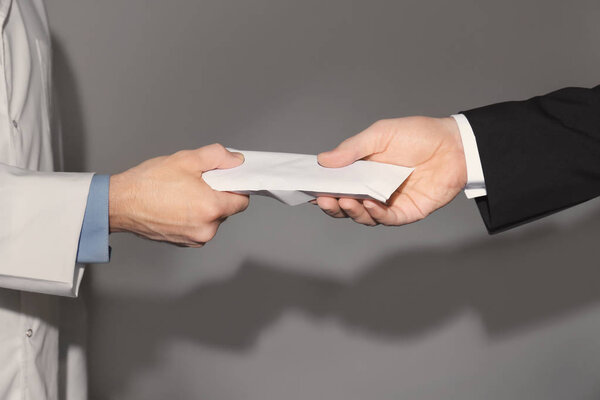 Врач получает взятку от бизнесмена на сером фоне, крупным планом
