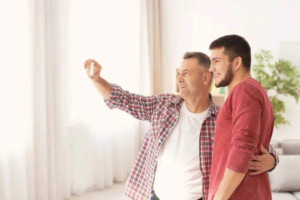 Hombre maduro tomando selfie con su hijo en casa — Foto de Stock