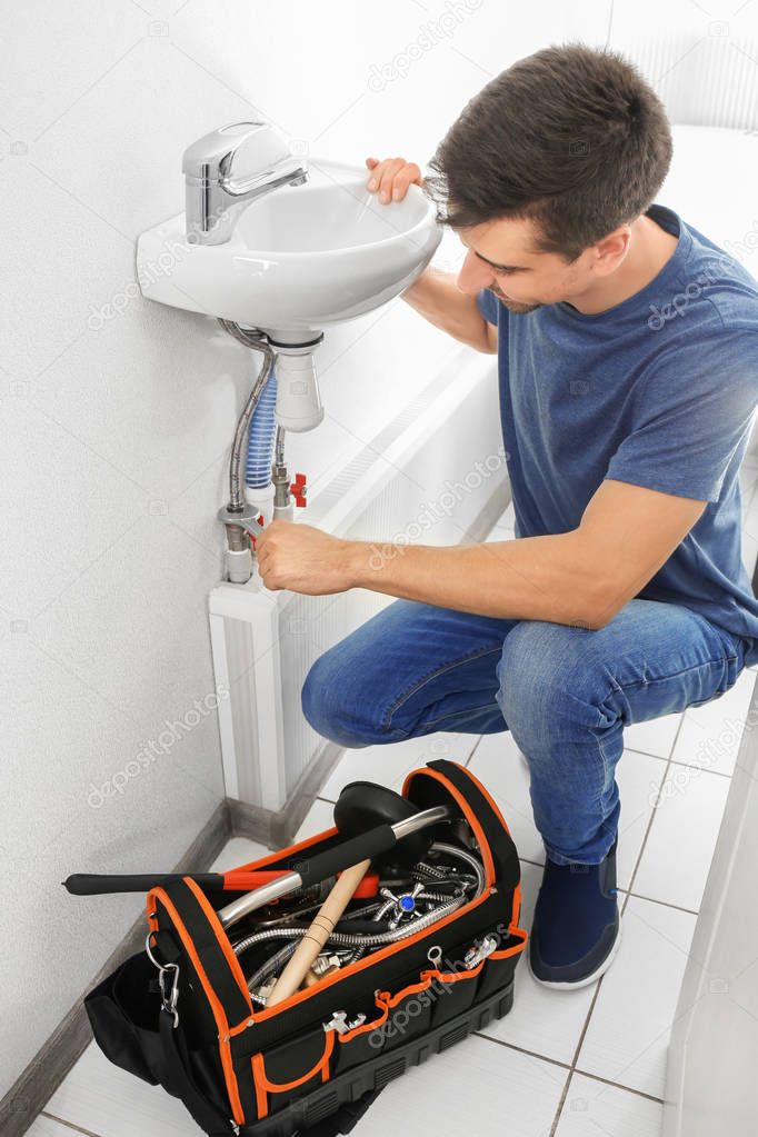 Young plumber repairing sink in bathroom