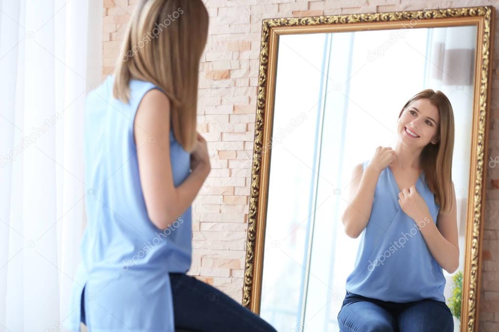 Young woman looking at herself in mirror indoors