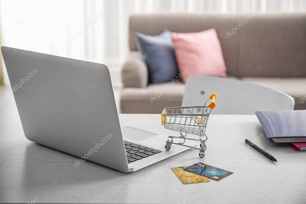 Laptop, small shopping trolley and credit cards on table. Internet shopping concept