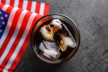 Glass of cold cola with flag of the USA on grey background clipart