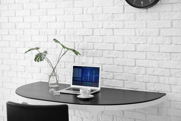 Comodo posto di lavoro a casa con computer portatile sulla scrivania contro muro di mattoni — Foto Stock