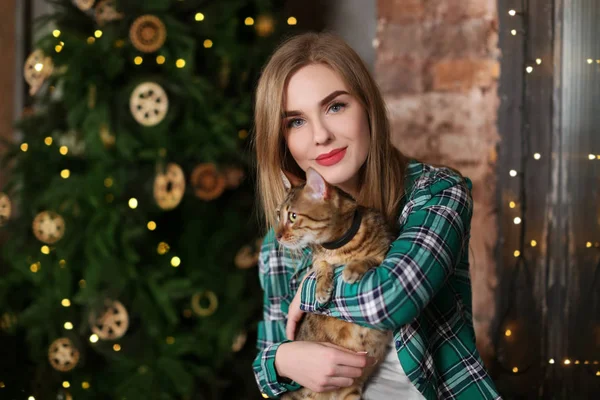 Mooie jonge vrouw met schattige kat in de buurt van de kerstboom thuis — Stockfoto