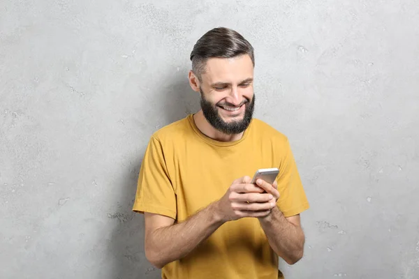 Портрет красивого мужчины с мобильным телефоном на сером фоне — стоковое фото