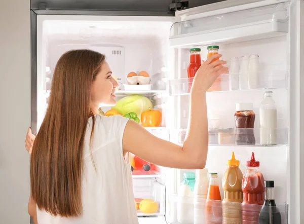 Женщина выбирает еду в холодильнике дома — стоковое фото