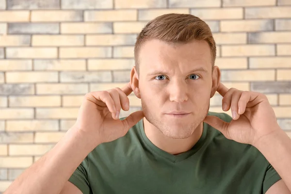 Young man with hearing problem on brick wall background — Stock Photo, Image