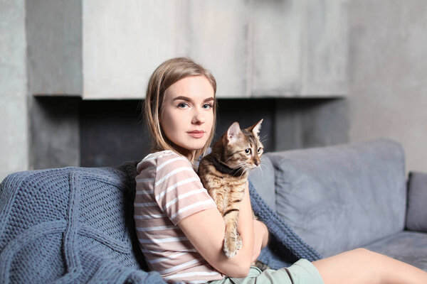 Beautiful young woman with cute cat on sofa at home