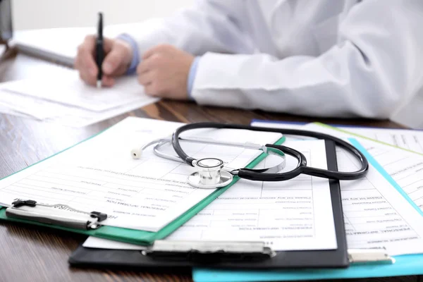 Clipboards with health insurance forms and doctor at table — Stock Photo, Image