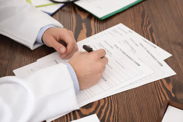 Médico preenchendo formulário de seguro à mesa — Fotografia de Stock