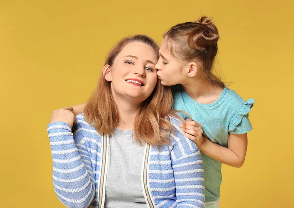 Menina bonito beijando sua mãe no fundo de cor — Fotografia de Stock