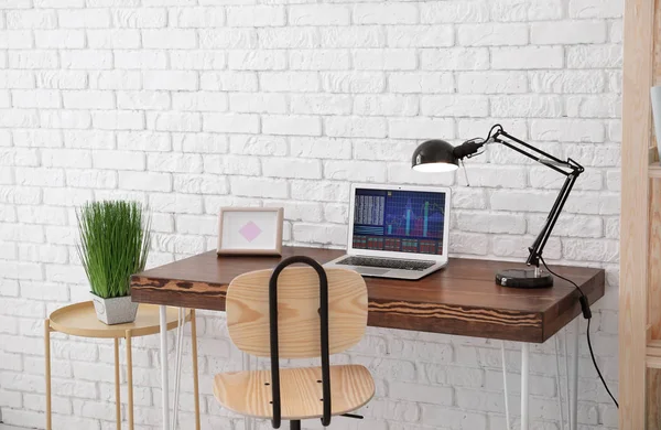 Komfortní domácí pracoviště s notebookem na stole proti cihlové zdi — Stock fotografie