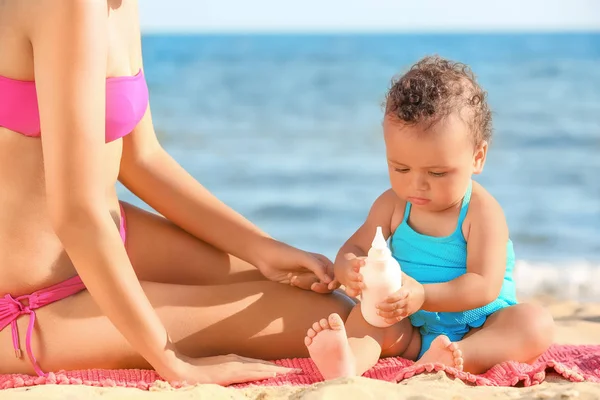 Young African American mother and daughter with suntan lotion on beach at resort — Stock Photo, Image