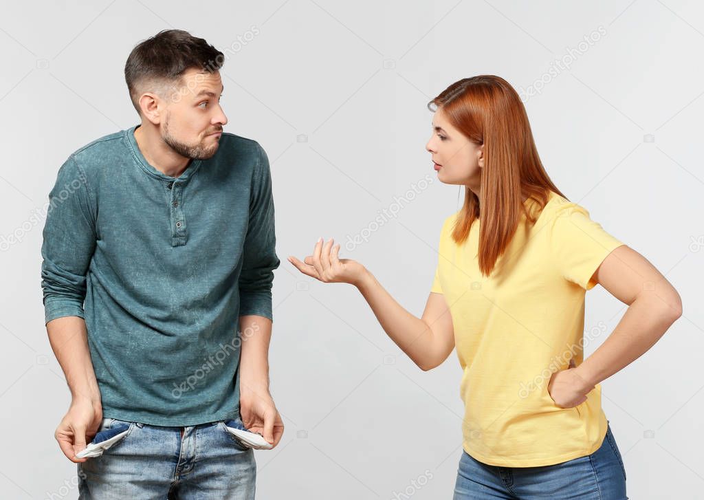 Woman demanding money from her husband who is showing empty pockets on light background