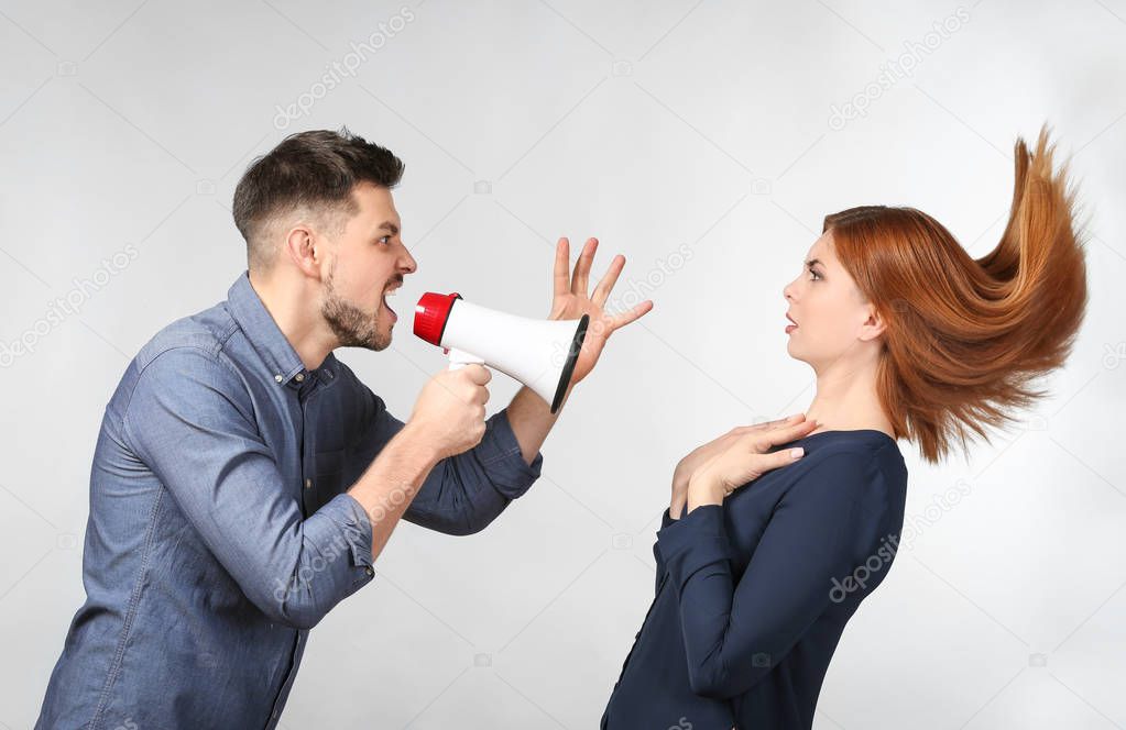 Angry man with megaphone scolding his wife on light background