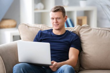 Genç adam kanepede kapalı dizüstü bilgisayar kullanarak