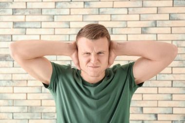 Kulakları tuğla duvar arka plan üzerinde kapsayan bir adam. İşitme sorunu