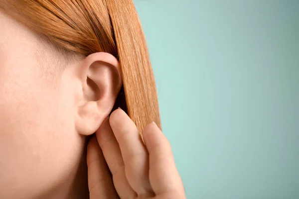 Young woman with hearing problem on color background, closeup