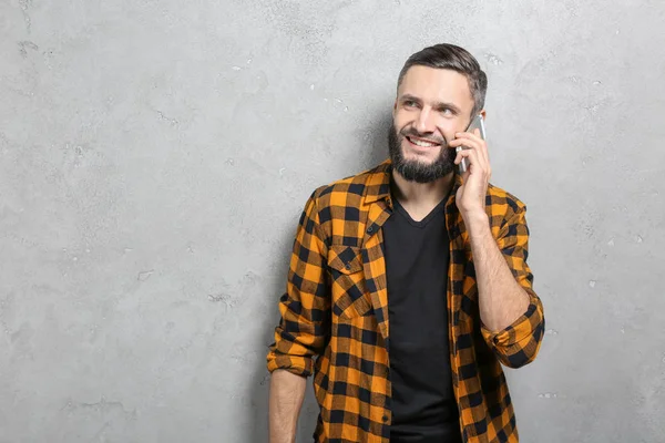 Jóképű férfi szürke háttér mobiltelefonon beszél — Stock Fotó