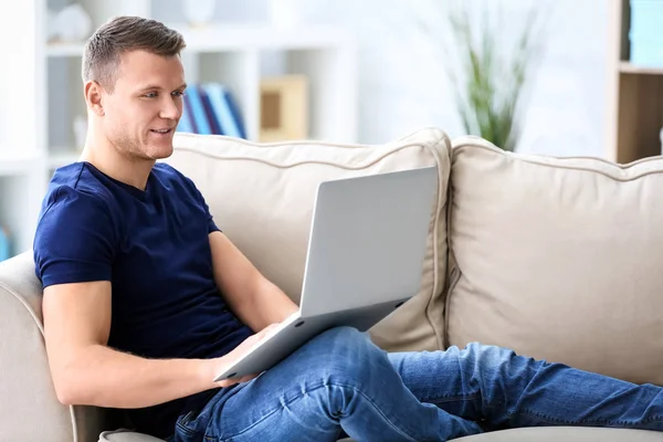 Молодой человек использует ноутбук на диване в помещении — стоковое фото