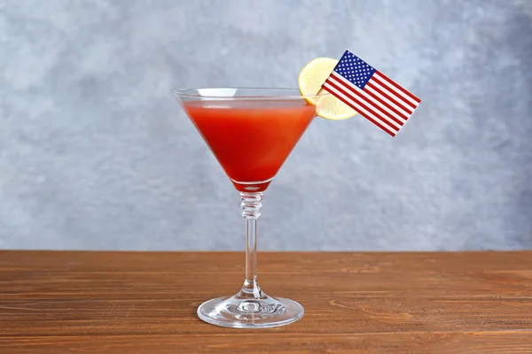 Glass of cocktail with small USA flag on table against grey background — Stock Photo, Image