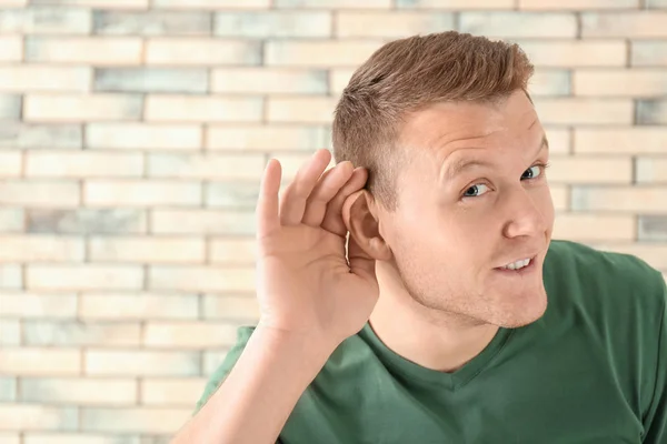 Giovane uomo con problemi di udito su sfondo muro di mattoni — Foto Stock