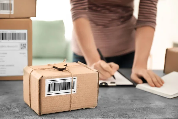 Parcel ready for shipment to customer and young woman working at table in home office. Startup business — Stock Photo, Image