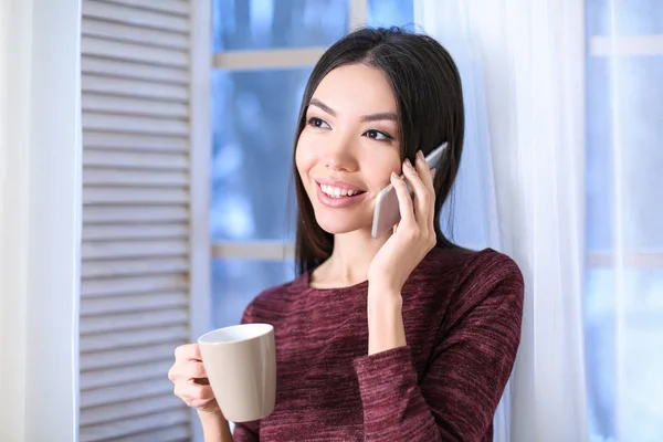 Hermosa mujer joven hablando por teléfono móvil y beber café en casa —  Fotos de Stock