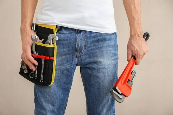 Jeune plombier avec ceinture à outils et clé à pipe sur fond clair — Photo