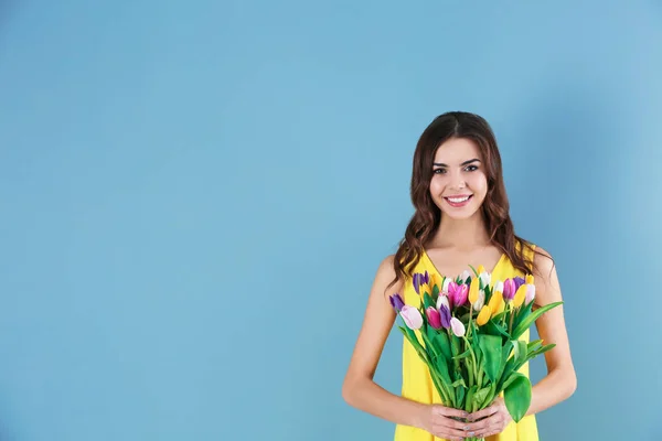 Hermosa mujer sosteniendo ramo de tulipanes sobre fondo de color — Foto de Stock