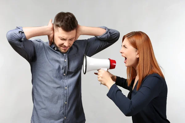 Angry woman with megaphone scolding her husband on light background — Stock Photo, Image