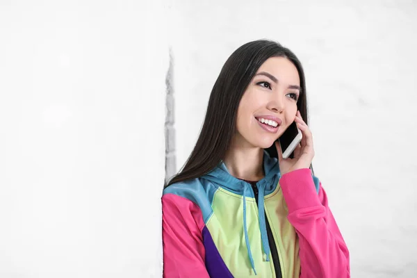 Красивая молодая женщина разговаривает по мобильному телефону возле белой стены — стоковое фото