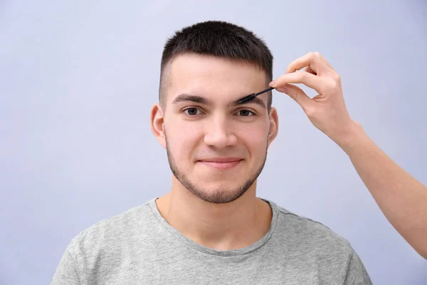 Maskenbildner färbt Augenbrauen auf dem Gesicht des Mannes vor hellem Hintergrund — Stockfoto