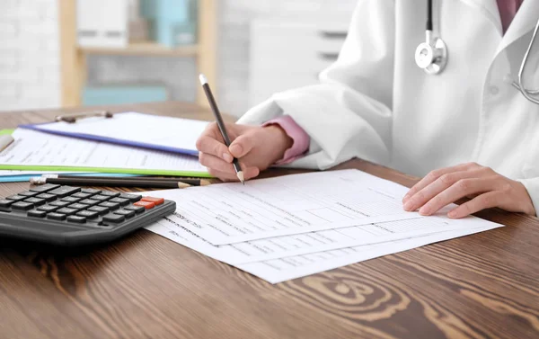 Médico preenchendo formulário de seguro à mesa — Fotografia de Stock