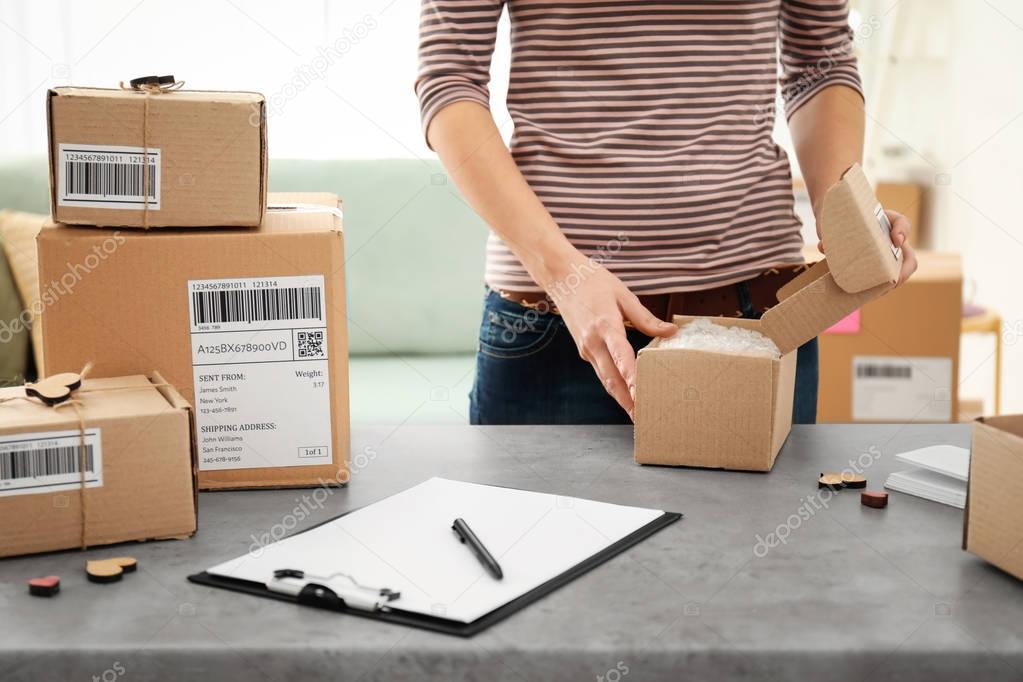 Young woman preparing parcels for shipment to customers at table in home office. Startup business