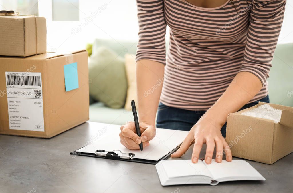 Young woman preparing parcels for shipment to customers at table in home office. Startup business