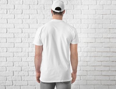 Tuğla duvar yakınındaki şık beyaz t-shirt yakışıklı genç adam. Mockup tasarım için