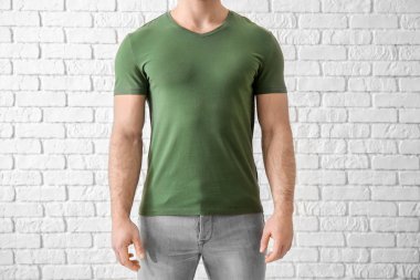 Young man in stylish t-shirt near white brick wall. Mockup for design clipart