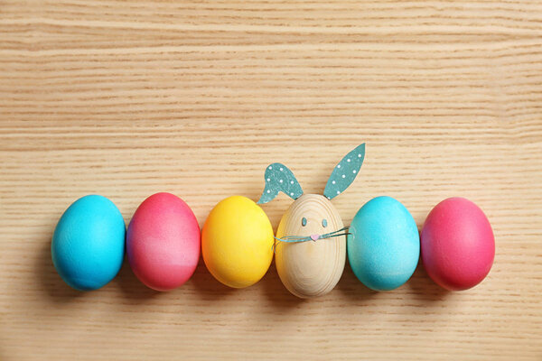 Colorful Easter eggs and one with bunny ears made from paper on wooden background