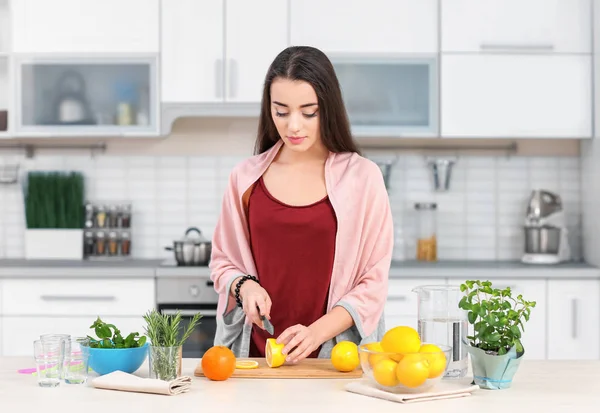 Νεαρή γυναίκα προετοιμασία νόστιμα λεμονάδα στην κουζίνα — Φωτογραφία Αρχείου