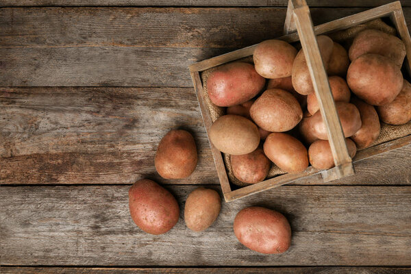 Wooden basket with fresh raw potatoes on table, top view