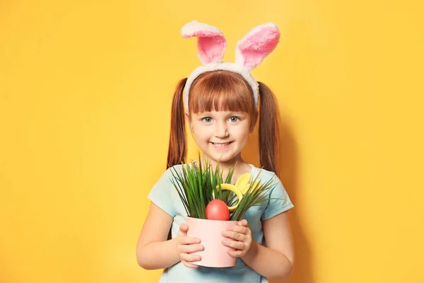 Menina bonito com orelhas de coelho segurando ovos de Páscoa em vaso de flores no fundo de cor — Fotografia de Stock