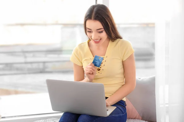 Mladá žena nakupování on-line s kreditní kartou a notebookem doma — Stock fotografie