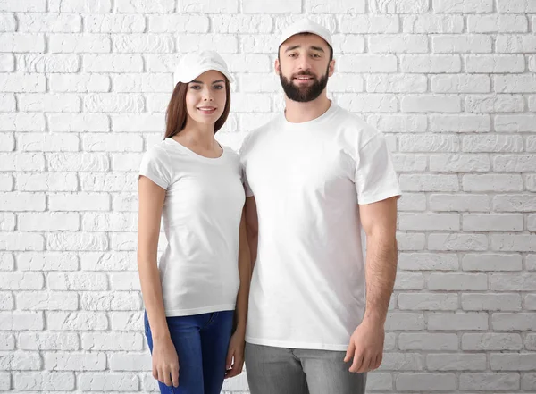 Jovem homem e mulher em elegantes camisetas brancas perto da parede de tijolo. Mockup para design — Fotografia de Stock